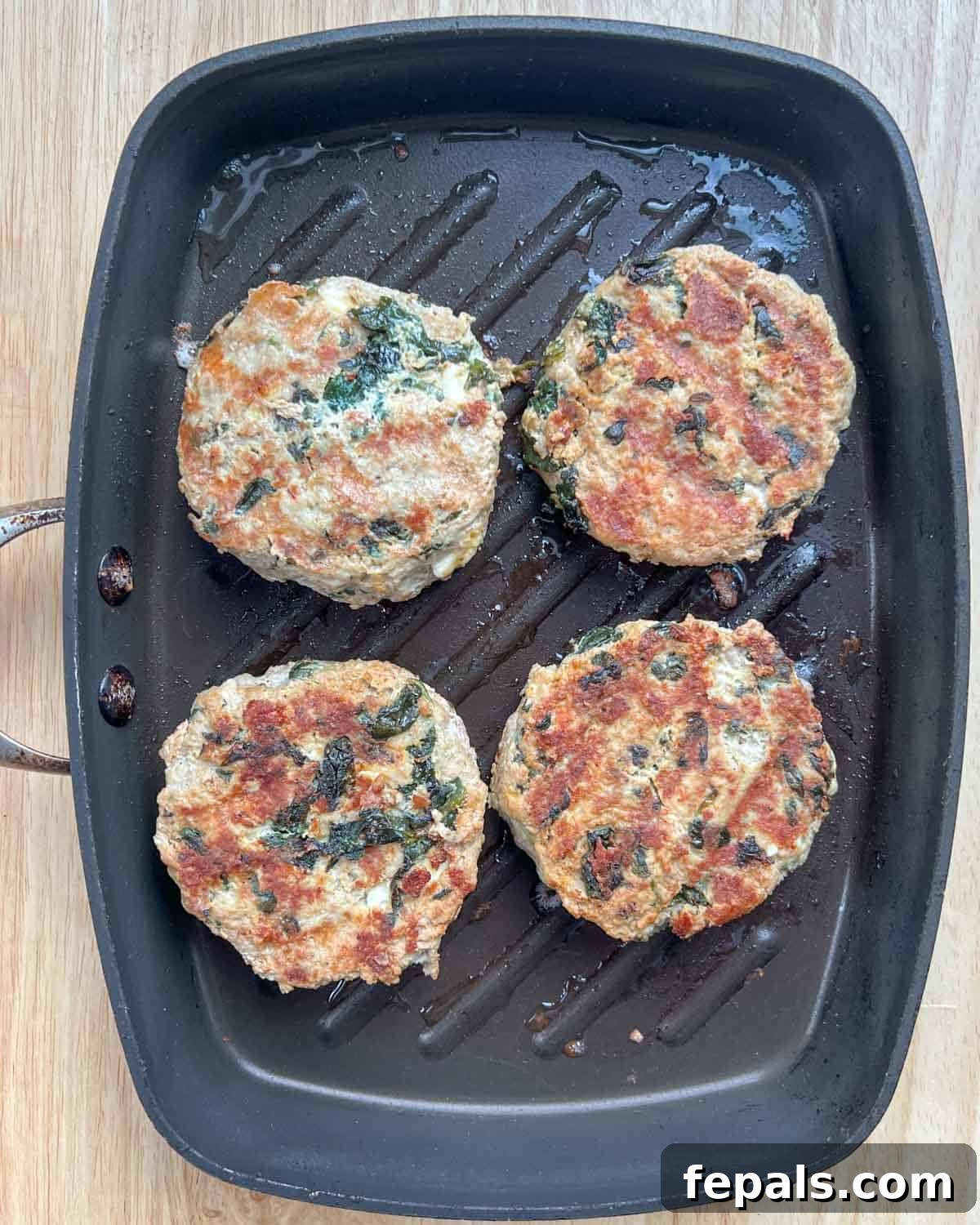 Gourmet Spinach and Feta Turkey Burgers 7 Four cooked turkey burger patties sizzling in a pan, golden brown and cooked through.