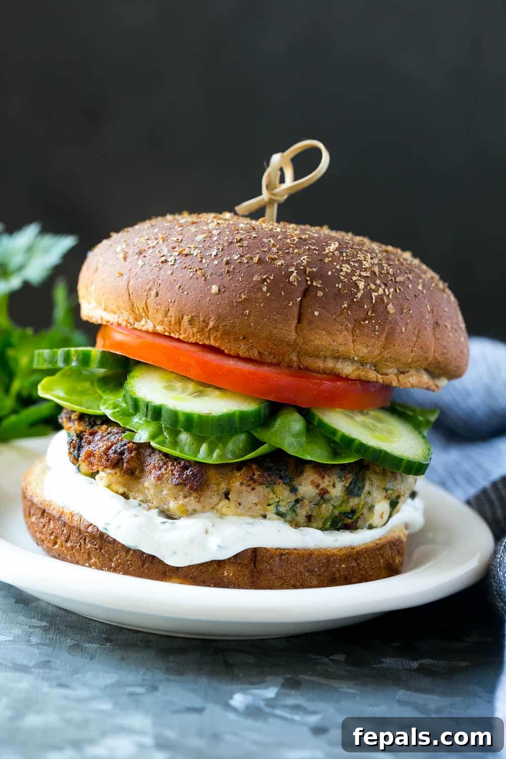 Spinach Feta Turkey Burger complete with fresh toppings and tzatziki A final presentation of a spinach and turkey feta burger on a plate, surrounded by fresh cucumber, lettuce, tomato, and a bowl of tzatziki sauce.