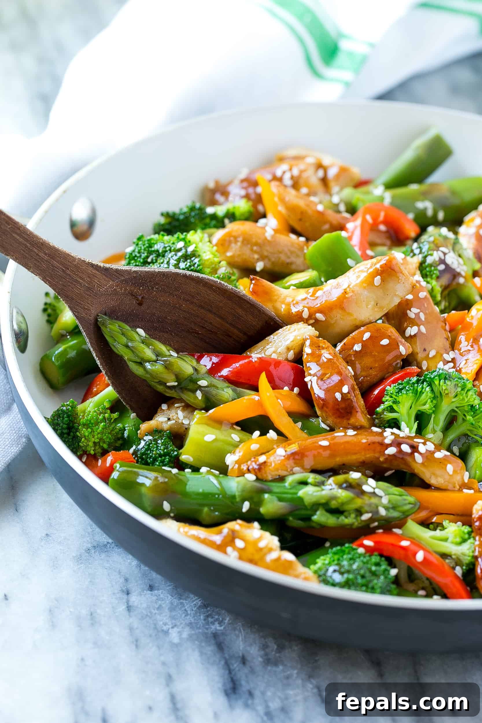 chicken stir fry recipe in skillet with wooden spoon and sesame seed