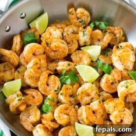 cilantro lime shrimp in a skillet cooked and garnished with lime wedges.