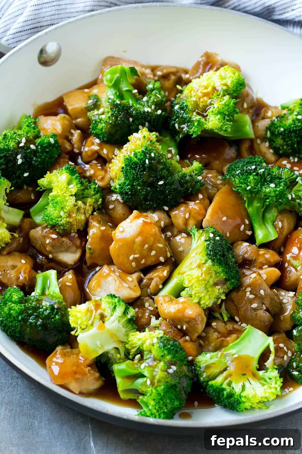 Easy and Healthy Chicken and Broccoli Stir-Fry Recipe Tender chicken and fresh broccoli in a skillet, coated in a sticky-sweet savory sauce and garnished with sesame seeds, ready to be served as a healthy and easy stir-fry dinner.