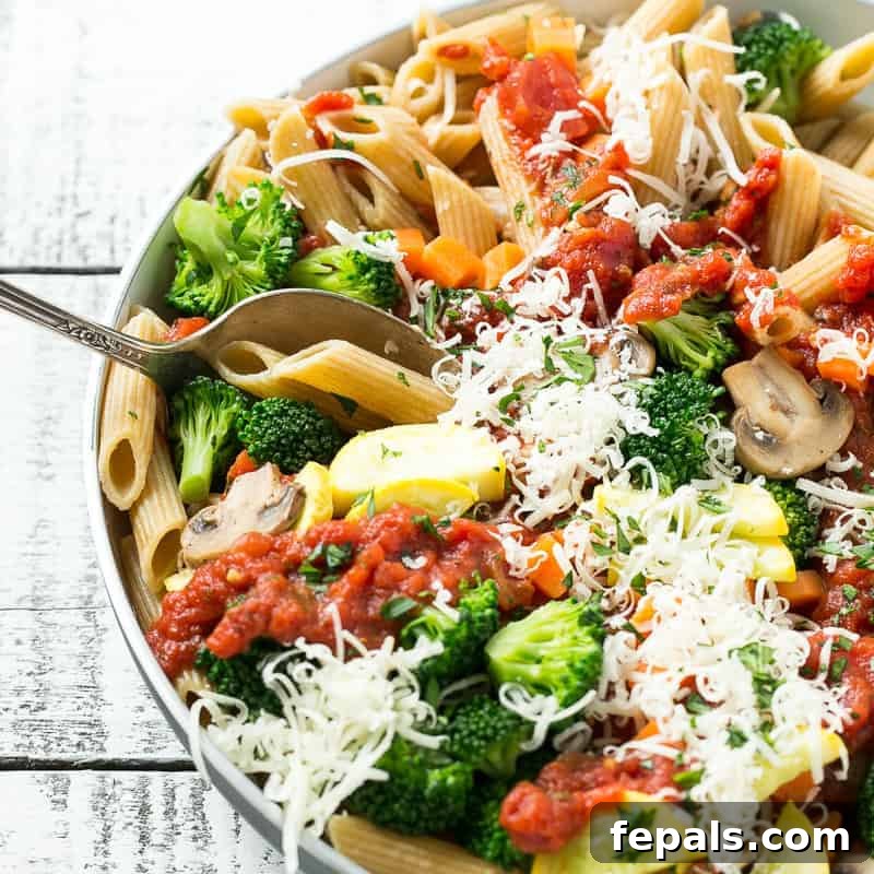 top view of a dish with pasta veggies and marinara sauce topped with shredded parmesan cheese