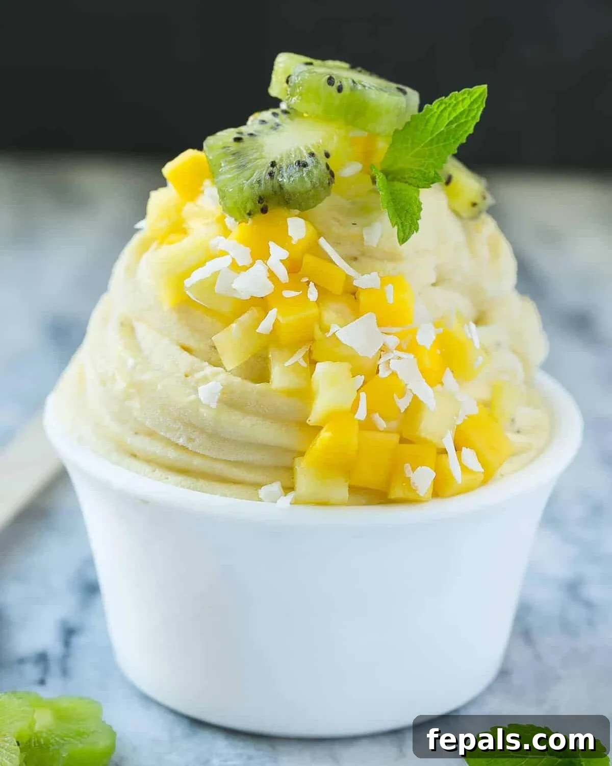 banana ice cream in a small round bowl topped with chopped fruits and shaved coconut.