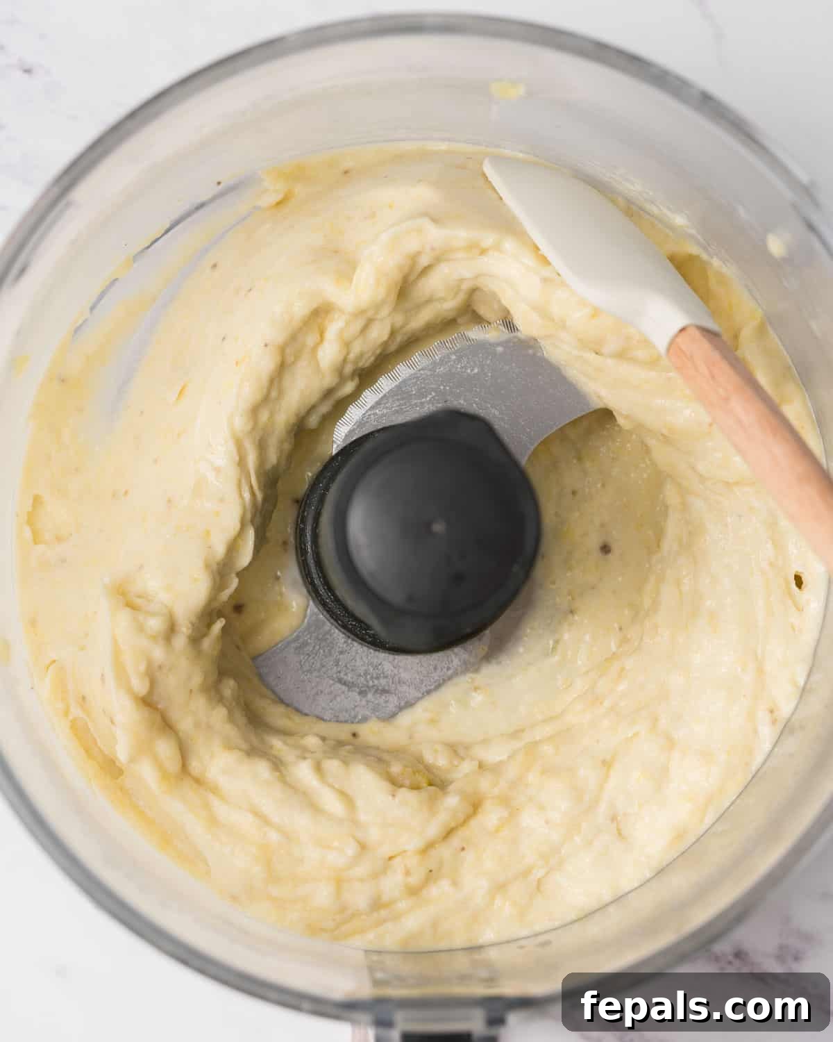 blended frozen fruits being scraped with a spatula from sides of the blender.