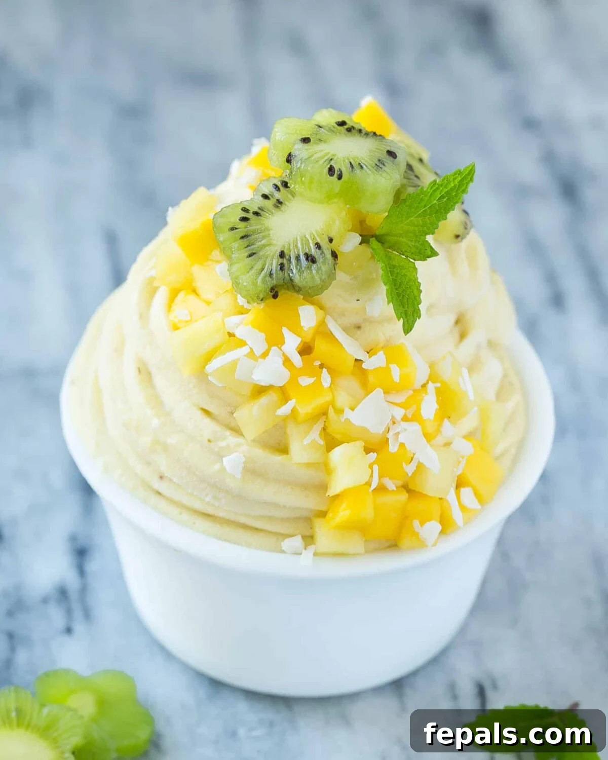 banana ice cream swirled into a white bowl topped with chopped fruits and fresh mint.