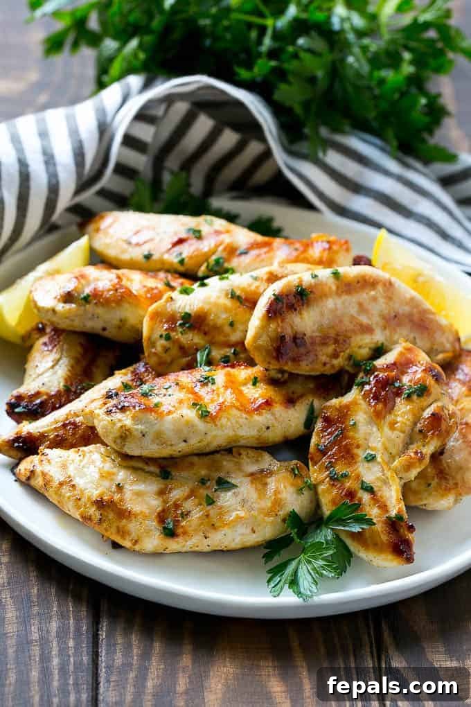 Zesty Lemon-Garlic Chicken Strips 3 Close-up side view of succulent lemon garlic chicken tenders, perfectly grilled and golden, presented on a pristine white plate.