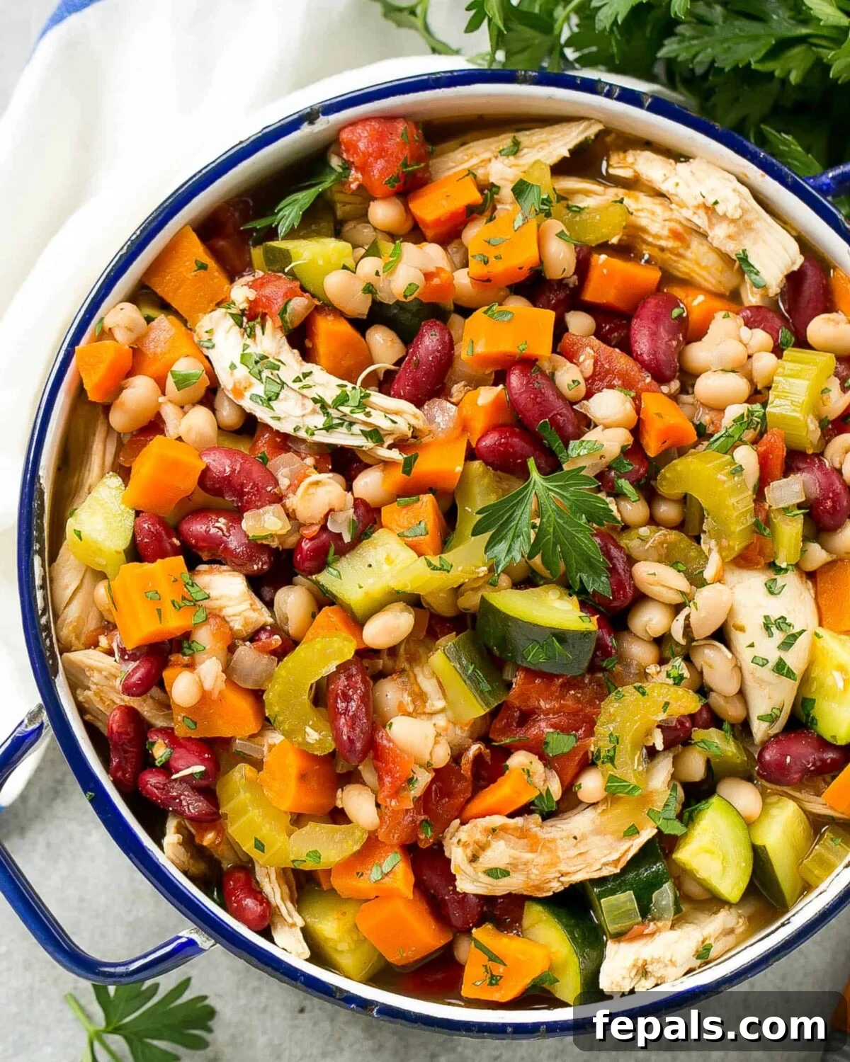 A round blue pot filled with hearty Italian chicken, bean, and vegetable soup, garnished with fresh parsley.
