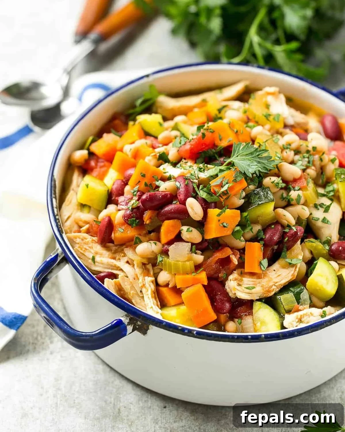 A large pot filled with a rich and colorful Italian chicken, bean, and vegetable soup, ready to be served.