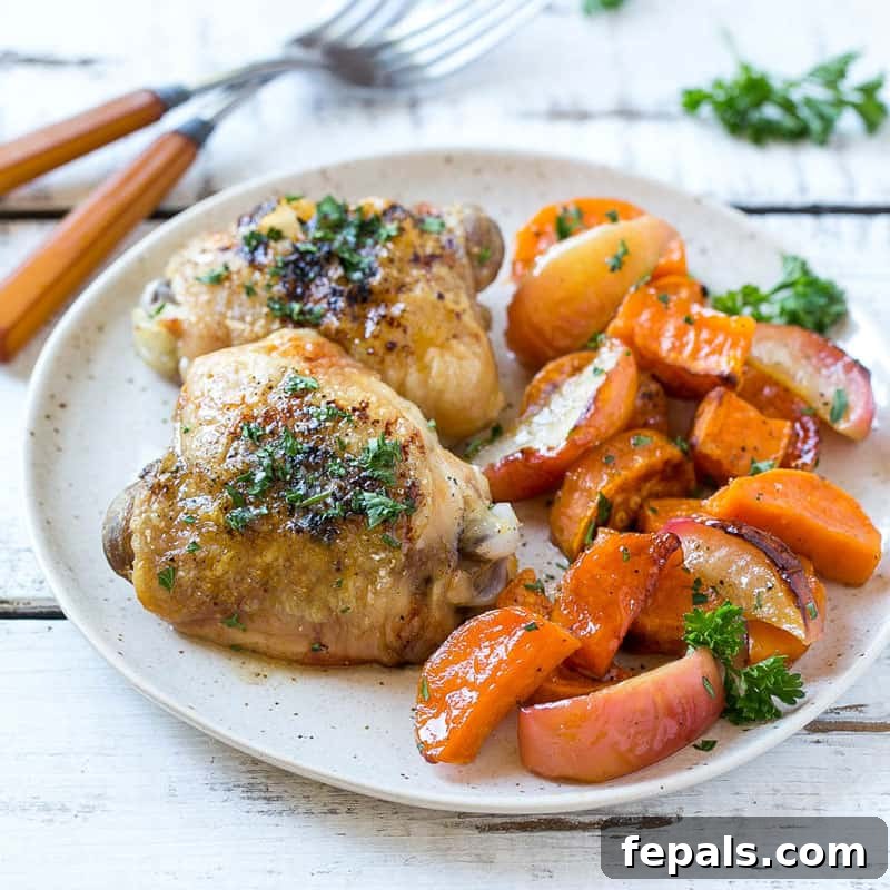 A final close-up of a plated serving of roasted chicken thigh, sweet potatoes, and apples with fresh herbs