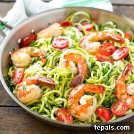 Vibrant Pesto Shrimp Zoodles 7 green-looking pesto zoodles topped with cooked shrimp and sliced tomatoes on a pan.