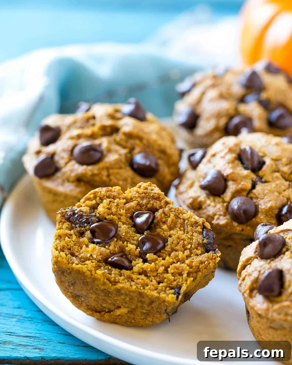 A side shot of a perfectly sliced pumpkin muffin on a white plate, revealing its moist interior and chocolate chips.