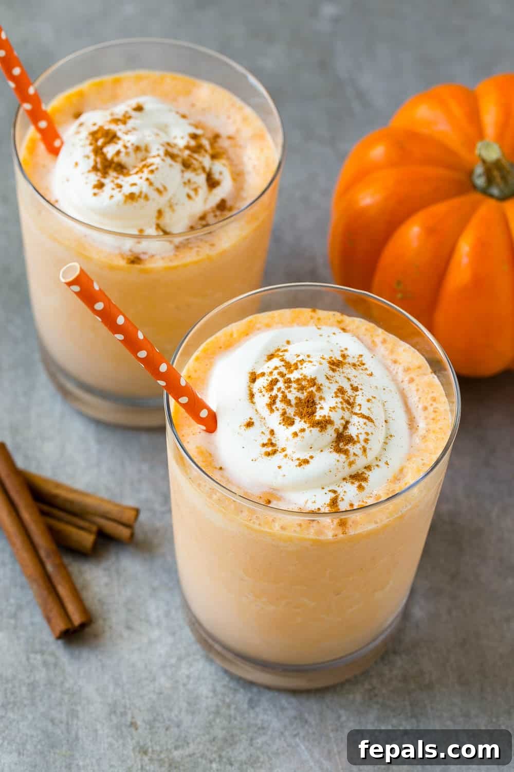 Pumpkin Spice Protein Power Smoothie 3 Two glasses of pumpkin pie protein smoothies, garnished with whipped cream and cinnamon, on a rustic surface.
