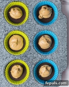 The protein-infused peanut butter mixture being carefully added over the chilled chocolate base in each mold, creating the middle layer.