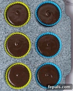 The final layer of melted chocolate being poured over the peanut butter filling in the molds, ready for chilling to create perfect protein peanut butter cups.