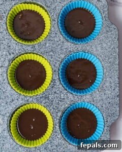 Melted chocolate neatly placed in the bottom of each silicone liner, forming the solid base of the peanut butter cups.