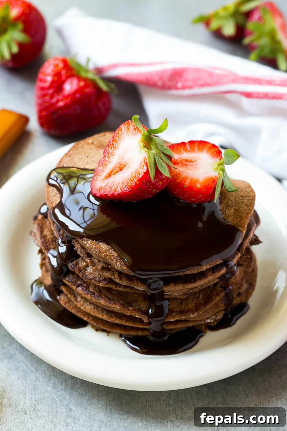 Stack of freshly cooked chocolate protein pancakes with a light dusting of cocoa powder and fresh mint garnish.