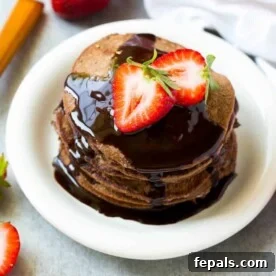 Top view of chocolate protein pancakes on a white plate topped with strawberries