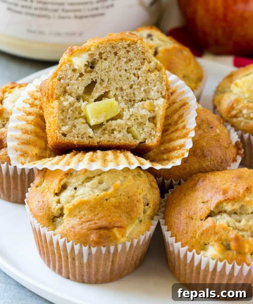 Power Apple Cinnamon Muffins 3 A perfectly sliced apple cinnamon muffin displaying its moist interior and apple chunks, resting on a white plate with other muffins in the background.