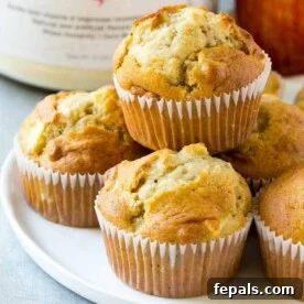 Power Apple Cinnamon Muffins 5 apple muffins stacked on a round white plate in front of a tub of protein powder