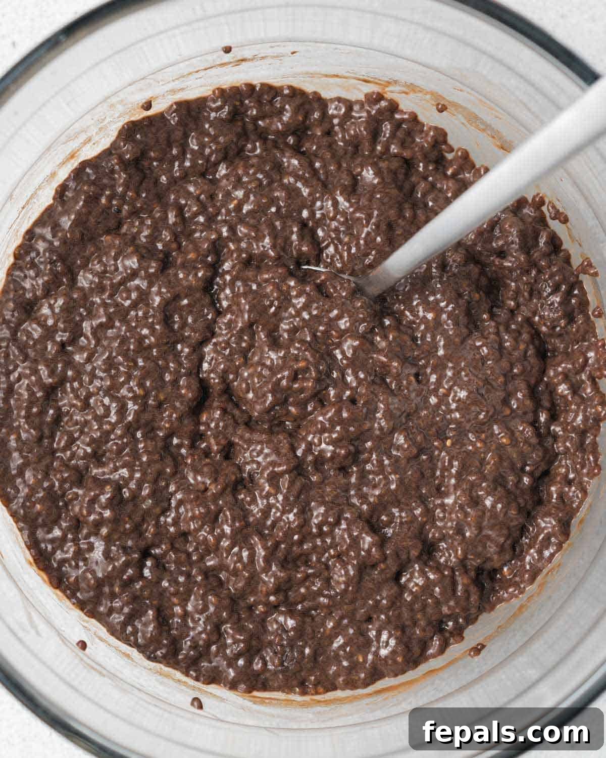 Decadent Chocolate Protein Chia Bliss 8 spoon mixing chia pudding in a clear bowl.