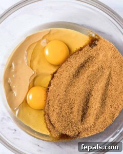 Power-Packed Protein Chocolate Cookies 17 Coconut sugar added over melted butter and 2 eggs in a clear bowl.