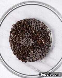 Coconut oil being poured over chocolate chips in a bowl for melting.