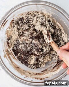 Hand mixing protein powder and almond flour with the chocolate mixture to create brownie batter.