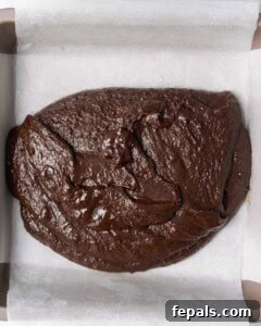 Brownie batter is poured into a lined baking pan and spread evenly.