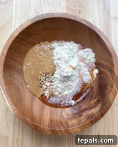 Oats, protein powder, peanut butter, and honey are added to a wooden bowl.