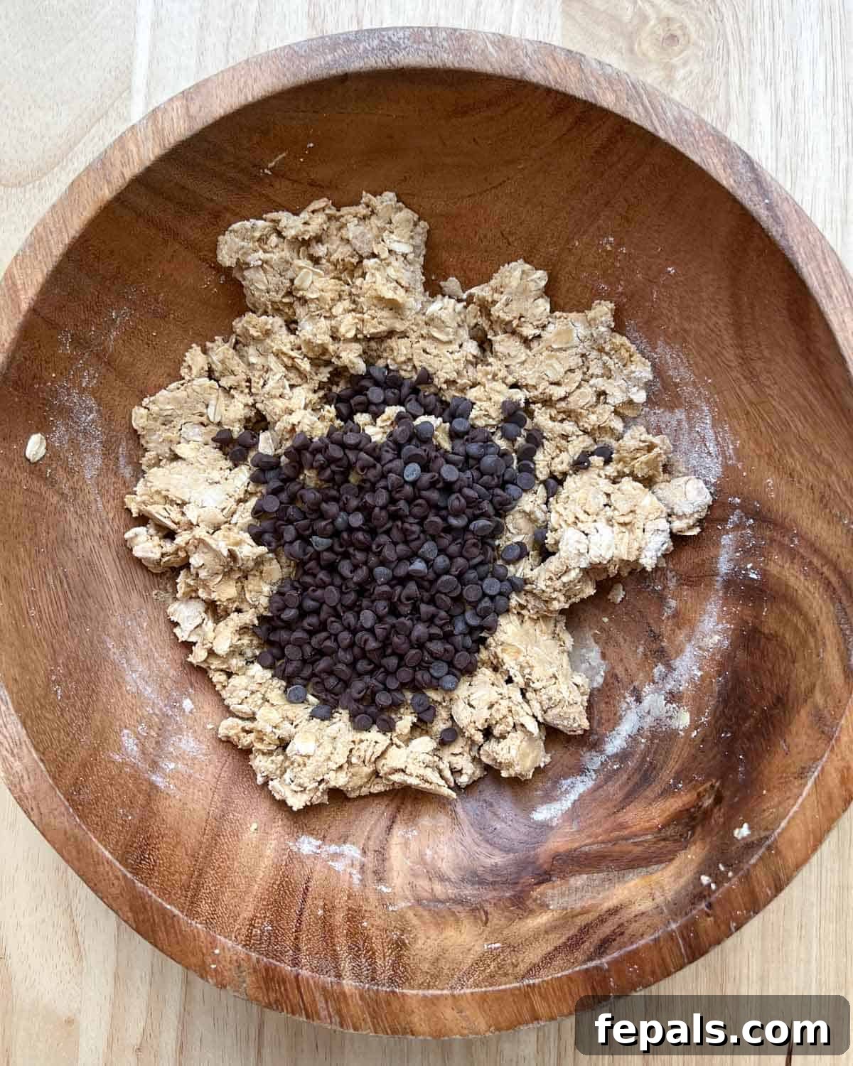Mini chocolate chips are gently added to the peanut butter and oats dough in the wooden bowl.