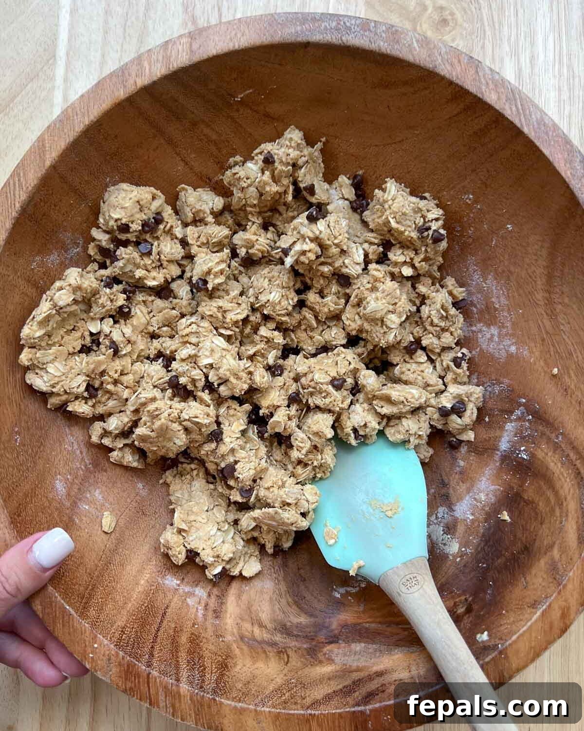 The chocolate chips are thoroughly mixed into the peanut butter and oats dough in a wooden bowl, creating a uniform mixture.