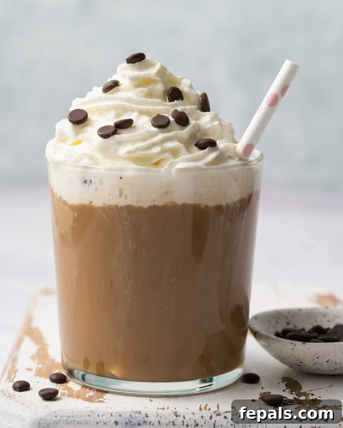 A delicious mocha brown protein smoothie in a clear glass cup, generously topped with fluffy whipped cream and a sprinkle of chocolate chips, ready to be enjoyed.