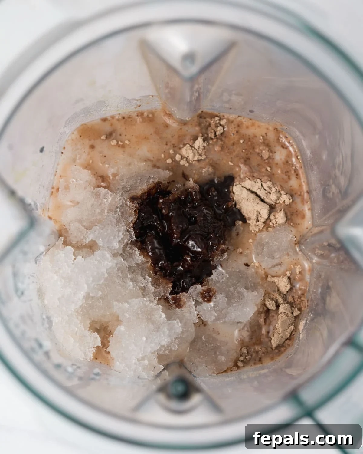 All the mocha protein shake ingredients, including chocolate protein powder, milk, coffee, and chocolate syrup, are carefully placed into a blender, ready for blending.
