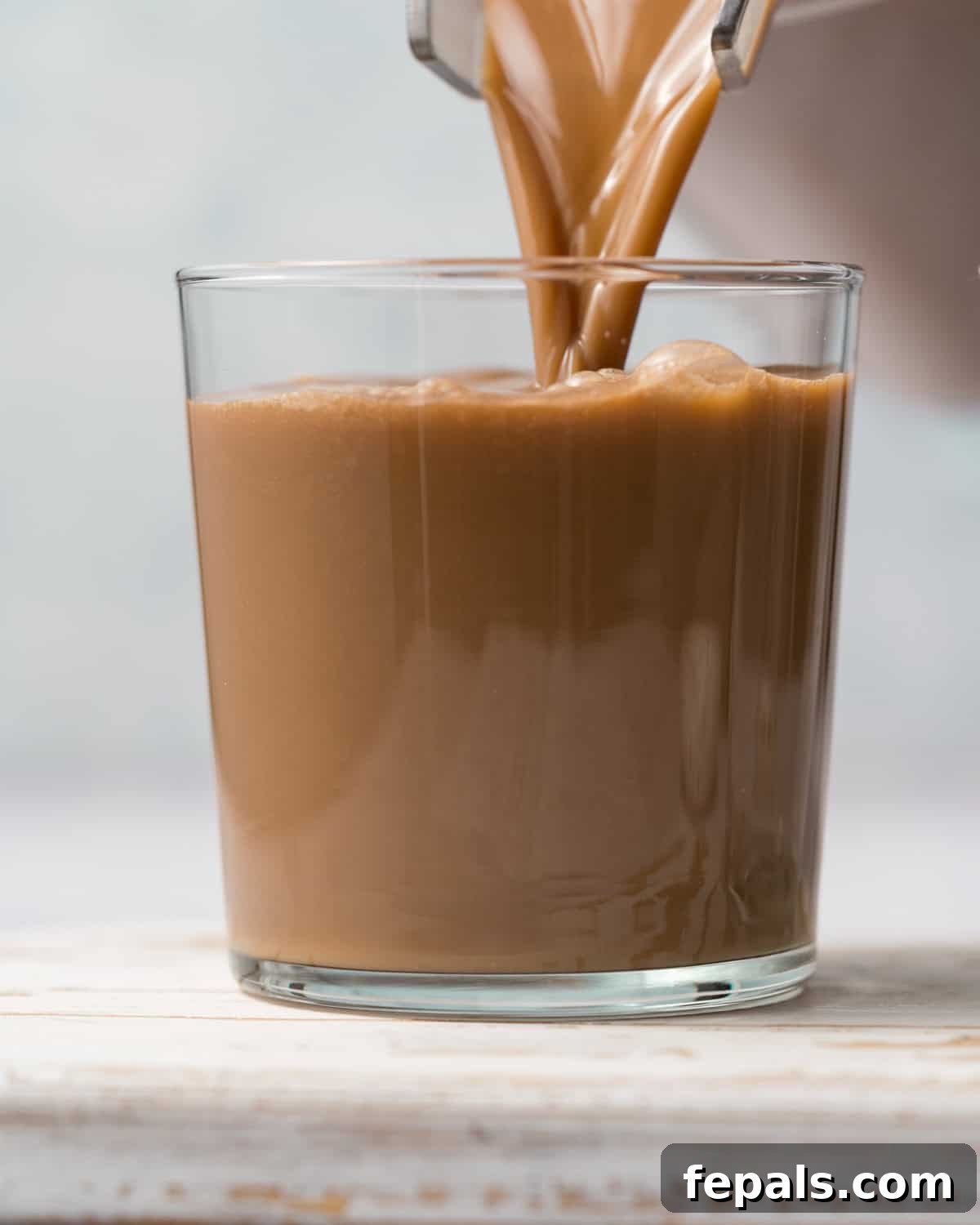 The freshly blended mocha protein shake is being poured into an elegant glass cup, showcasing its rich, inviting color and smooth texture.
