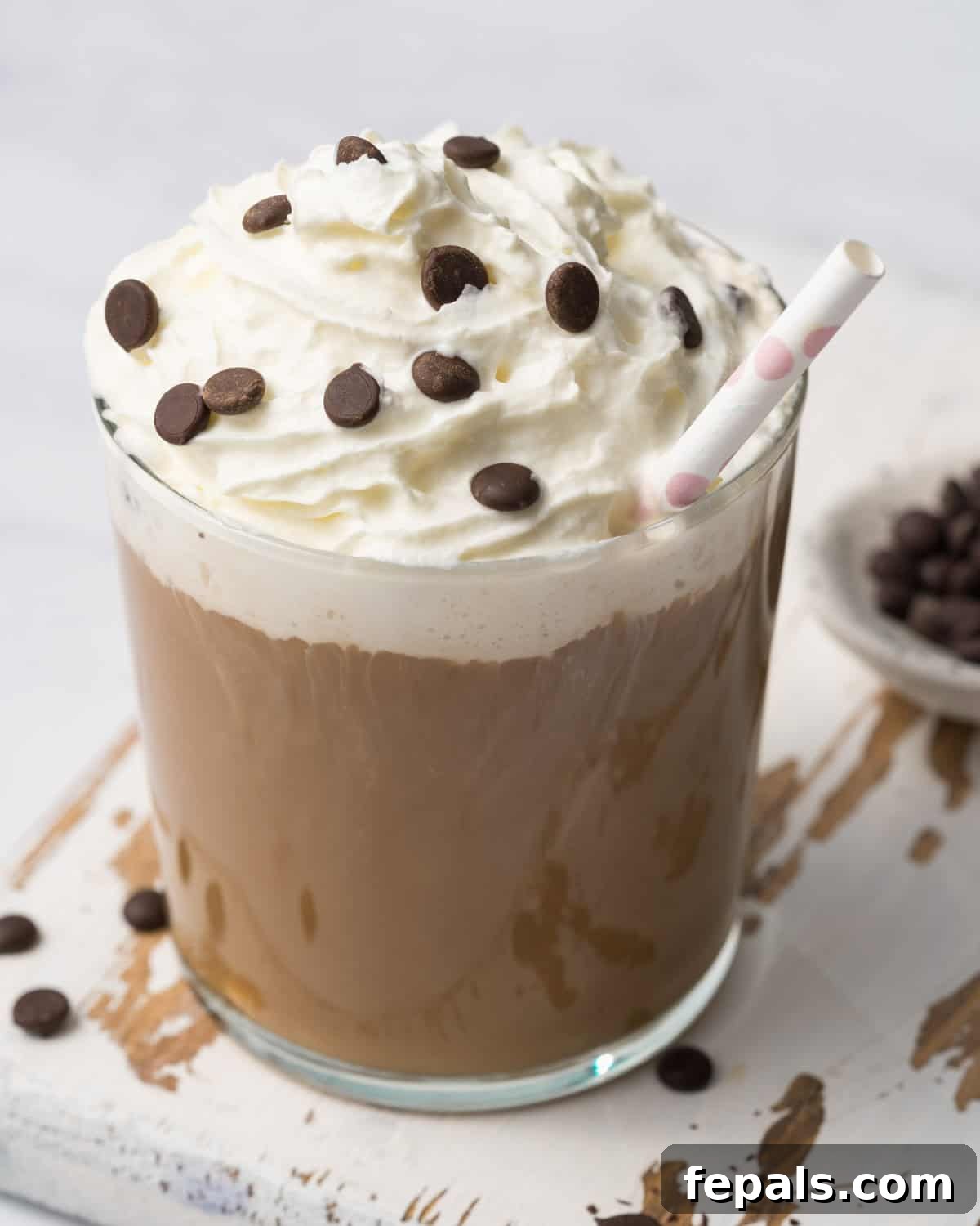 A beautifully presented mocha shake in a clear glass cup, adorned with whipped cream and chocolate chips, with a straw inserted, ready for a delightful indulgence.