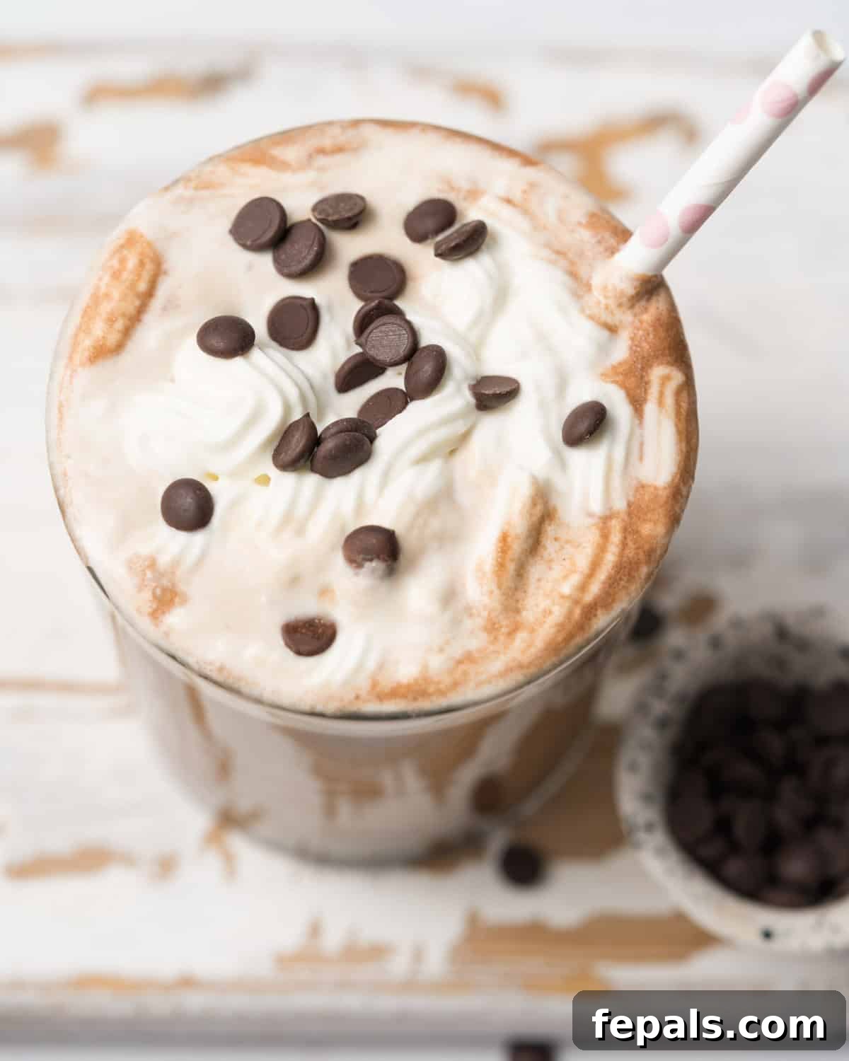 A close-up view of a mocha protein shake, highlighting the luscious whipped cream topping adorned with scattered chocolate chips, with a straw inviting a sip.