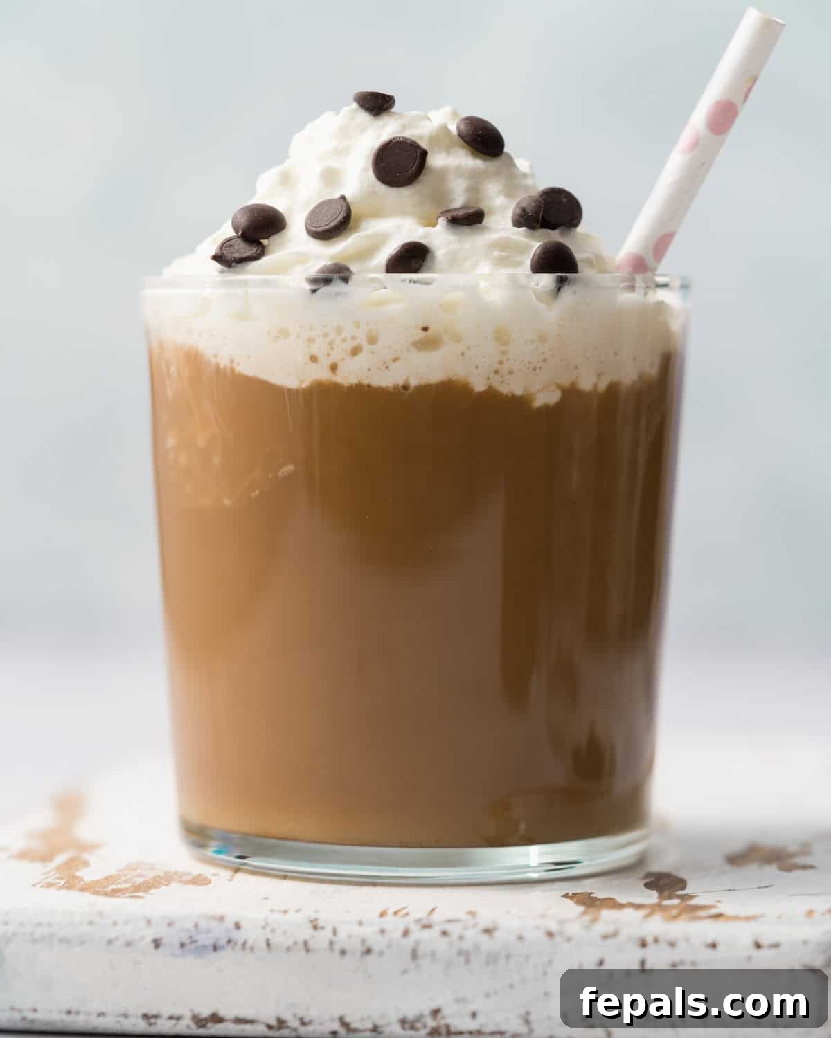 A tall glass cup filled with a smooth mocha smoothie, topped generously with whipped cream and a straw, presented against a soft, inviting background.