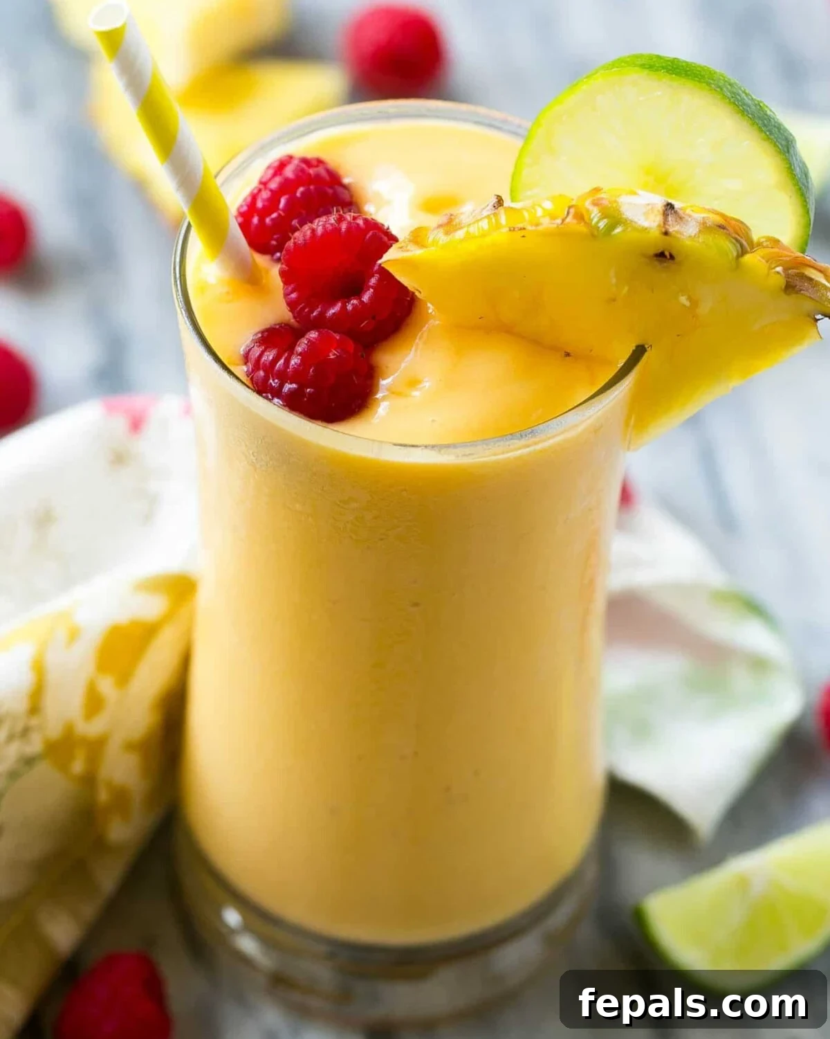 Tropical Escape Protein Smoothie 2 Vibrant yellow tropical smoothie in a clear glass, topped with fresh raspberries for garnish.