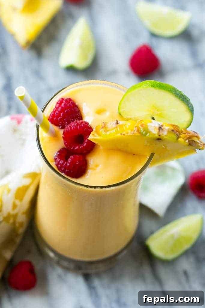 Tropical Escape Protein Smoothie 3 A tall glass filled with a creamy tropical protein smoothie, garnished with a pineapple slice and raspberries, with a straw.