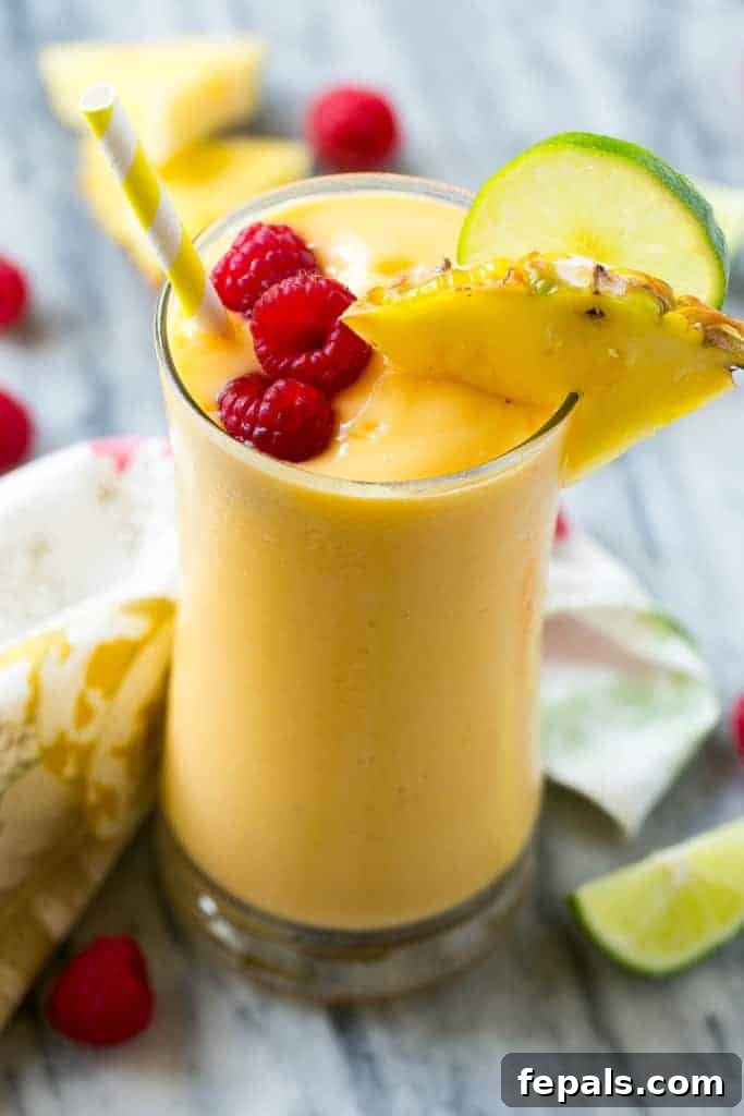 Tropical Escape Protein Smoothie 4 A refreshing tropical smoothie in a cup with a straw, garnished with a raspberry and a slice of pineapple.