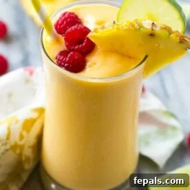 Vibrant yellow tropical smoothie in a clear glass, topped with fresh raspberries for garnish.