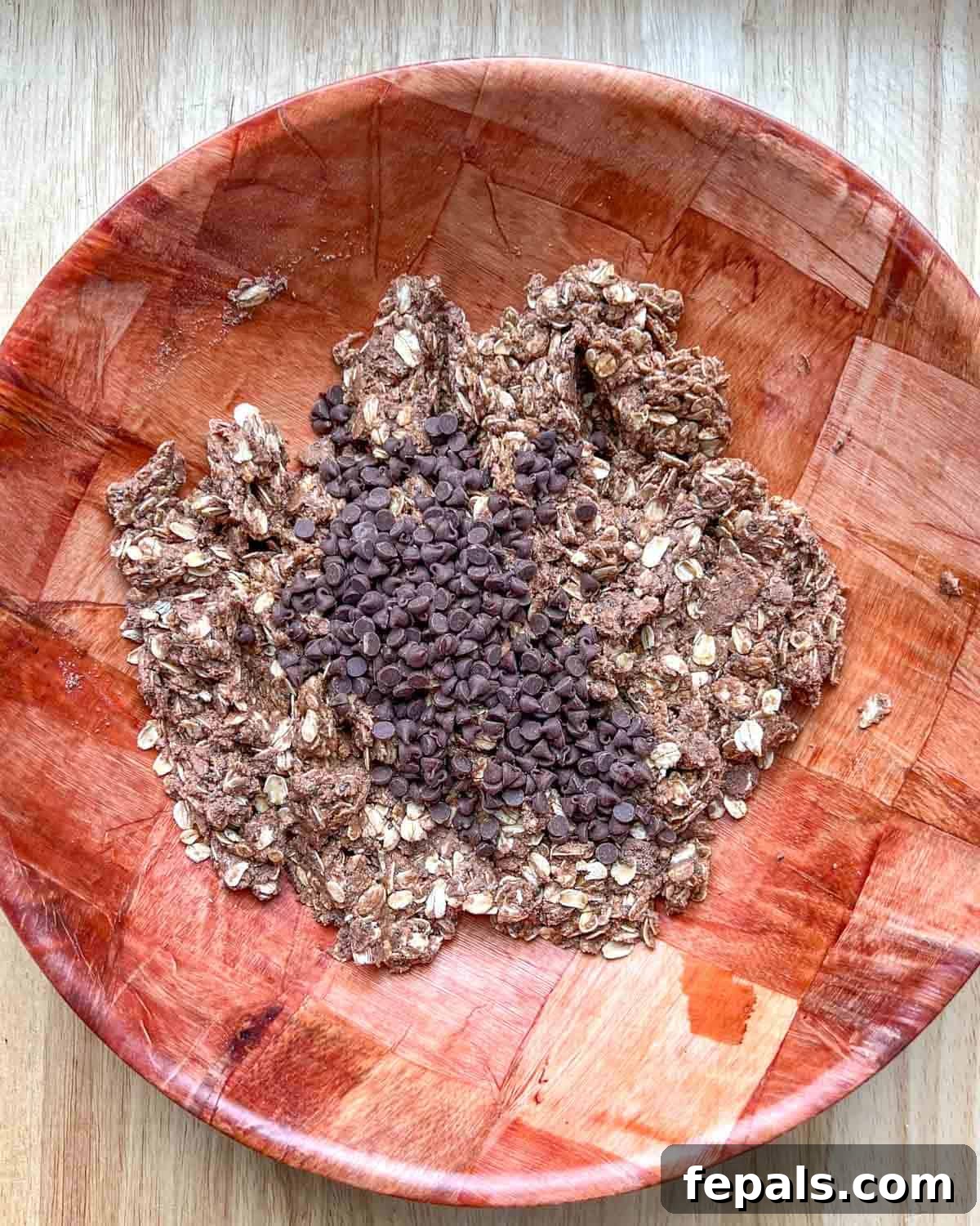 Mini chocolate chips generously added over the prepared peanut butter oat dough mixture in a bowl.