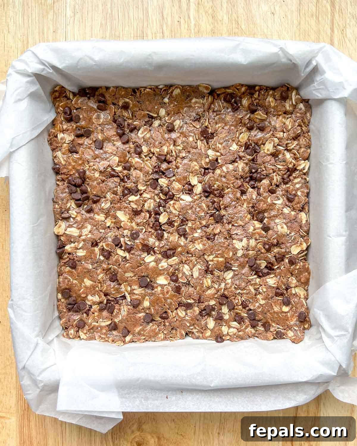 The protein bar dough firmly pressed into a pan lined with parchment paper, creating a smooth, even surface.