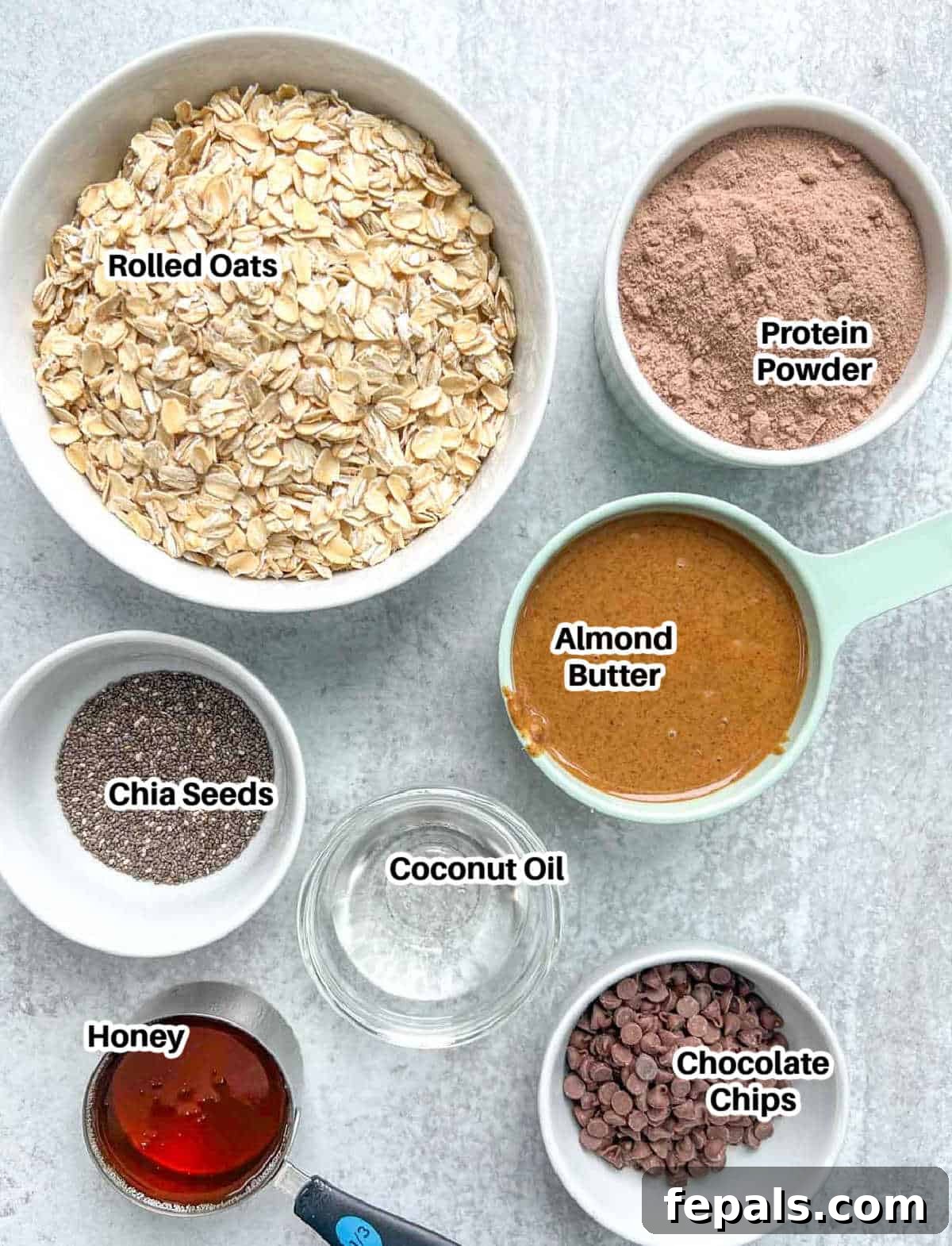 A selection of raw ingredients including rolled oats, protein powder, nut butter, and honey, ready to make chocolate protein bars.