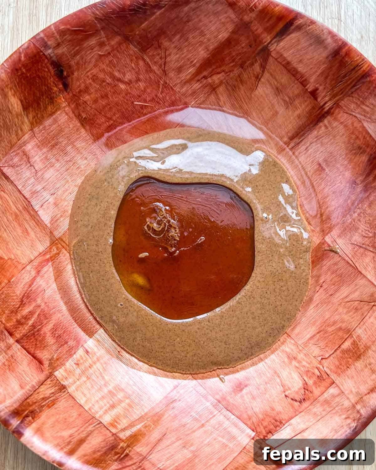 A brown bowl containing creamy almond butter, melted coconut oil, and golden honey.