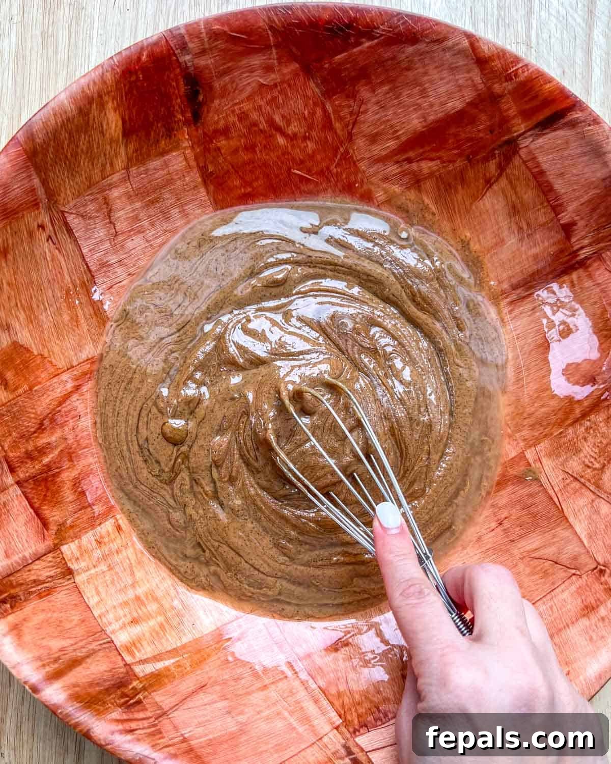 A whisk vigorously mixing the smooth blend of nut butter, honey, and coconut oil.