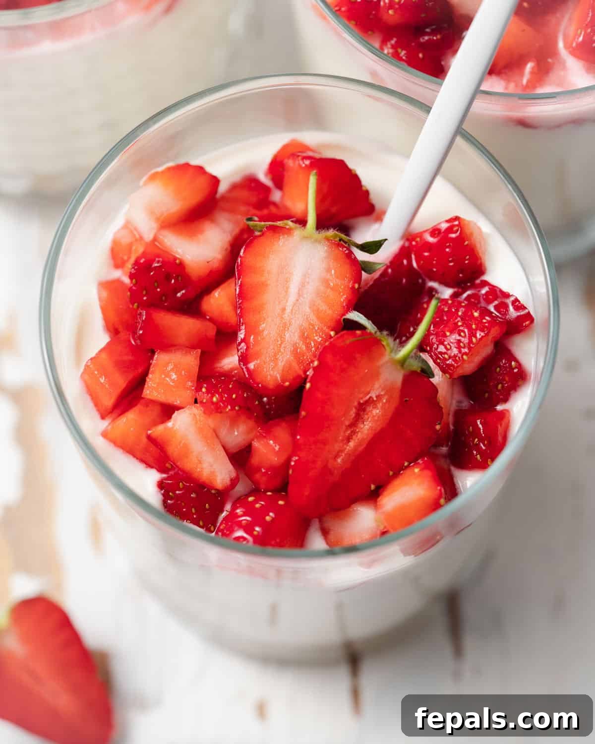 A single clear cup containing a no-bake cheesecake, beautifully topped with an abundance of fresh, chopped strawberries.