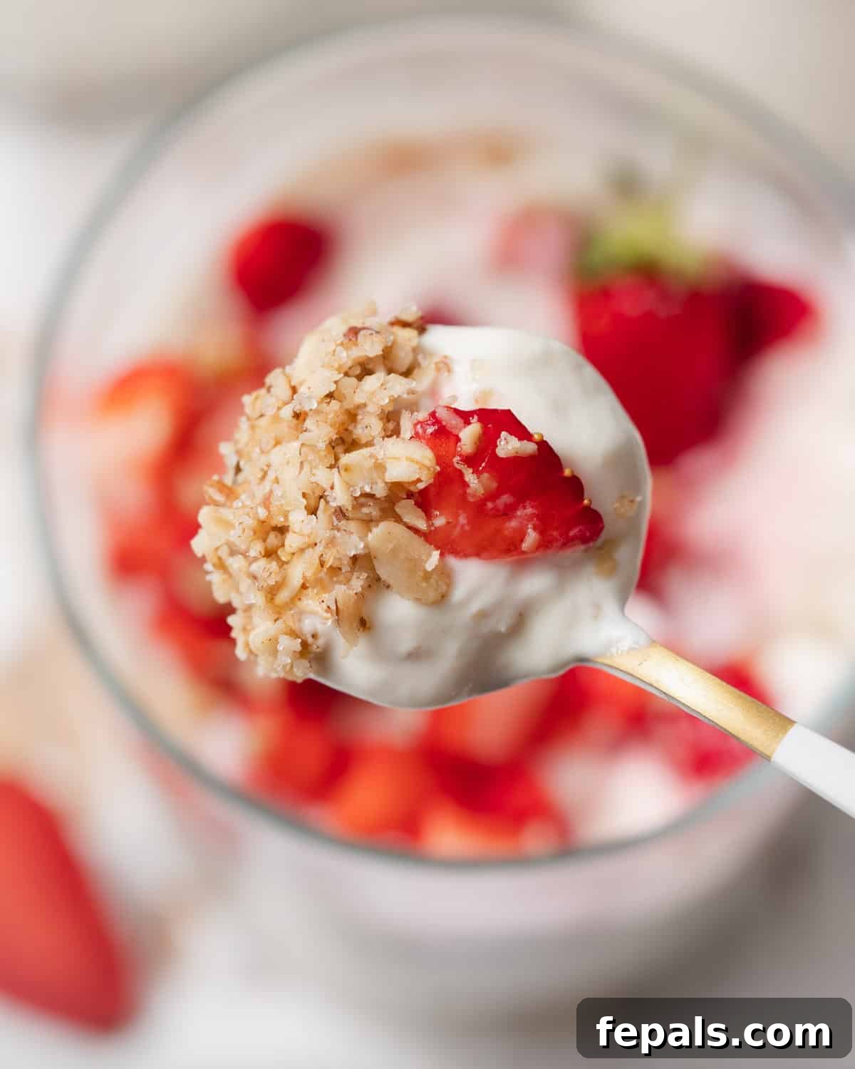 A spoon taking a generous spoonful of no-bake cheesecake from a cup, showcasing the creamy filling and a fresh strawberry topping.