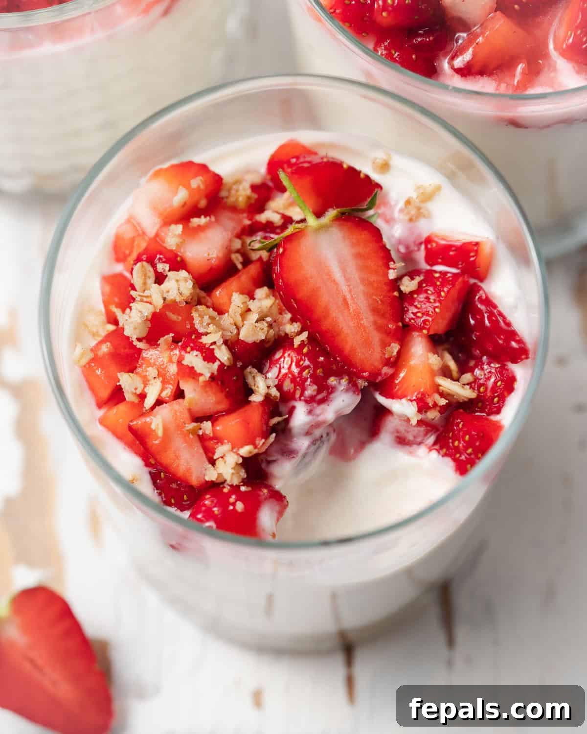 A clear cup of no-bake cheesecake, with a bite taken out, showing the layers and fresh chopped strawberries on top.