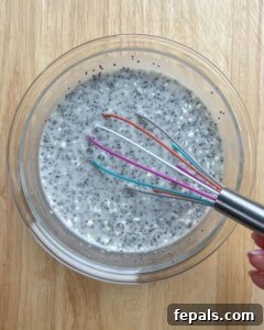 Creamy Coconut Chia Seed Pudding 6 chia seeds mixed with coconut milk, maple syrup, and protein powder in a bowl with whisk in a bowl.